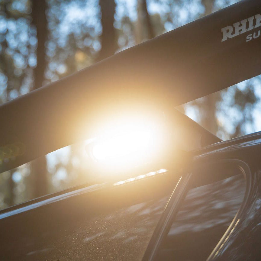 Work light lit up on a vehicle bar among trees, giving a bright warm glow