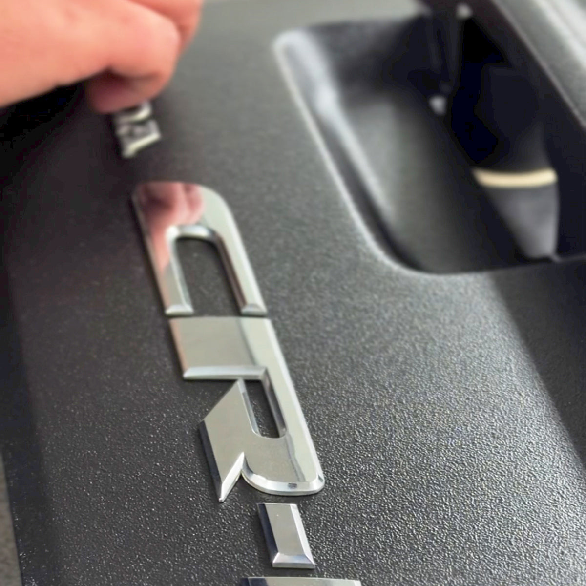 Black textured plastic trim with a chrome badge finished in TXT aerosol