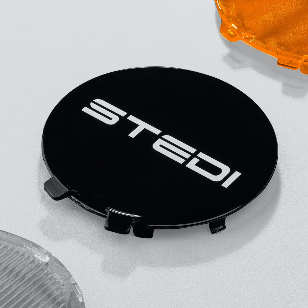 Black cover lying on a grey surface with the white STEDI logo, an amber cover just in frame at the top corner