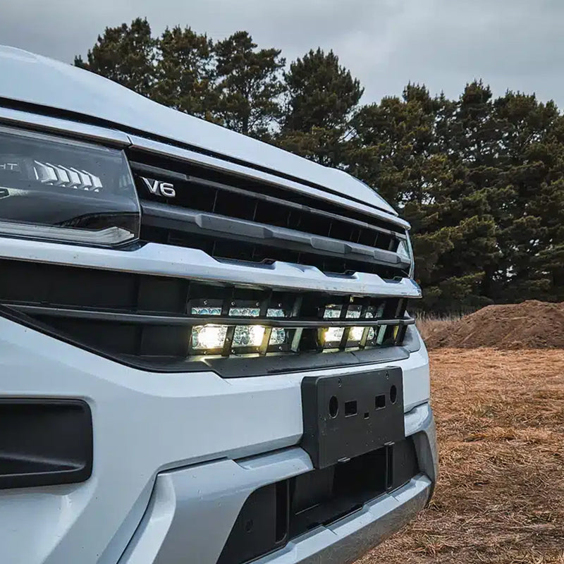 VW Amarok behind-grille LED light bar kit with one long bar and two compact light bars in black housings with clear lenses. installed to the car 