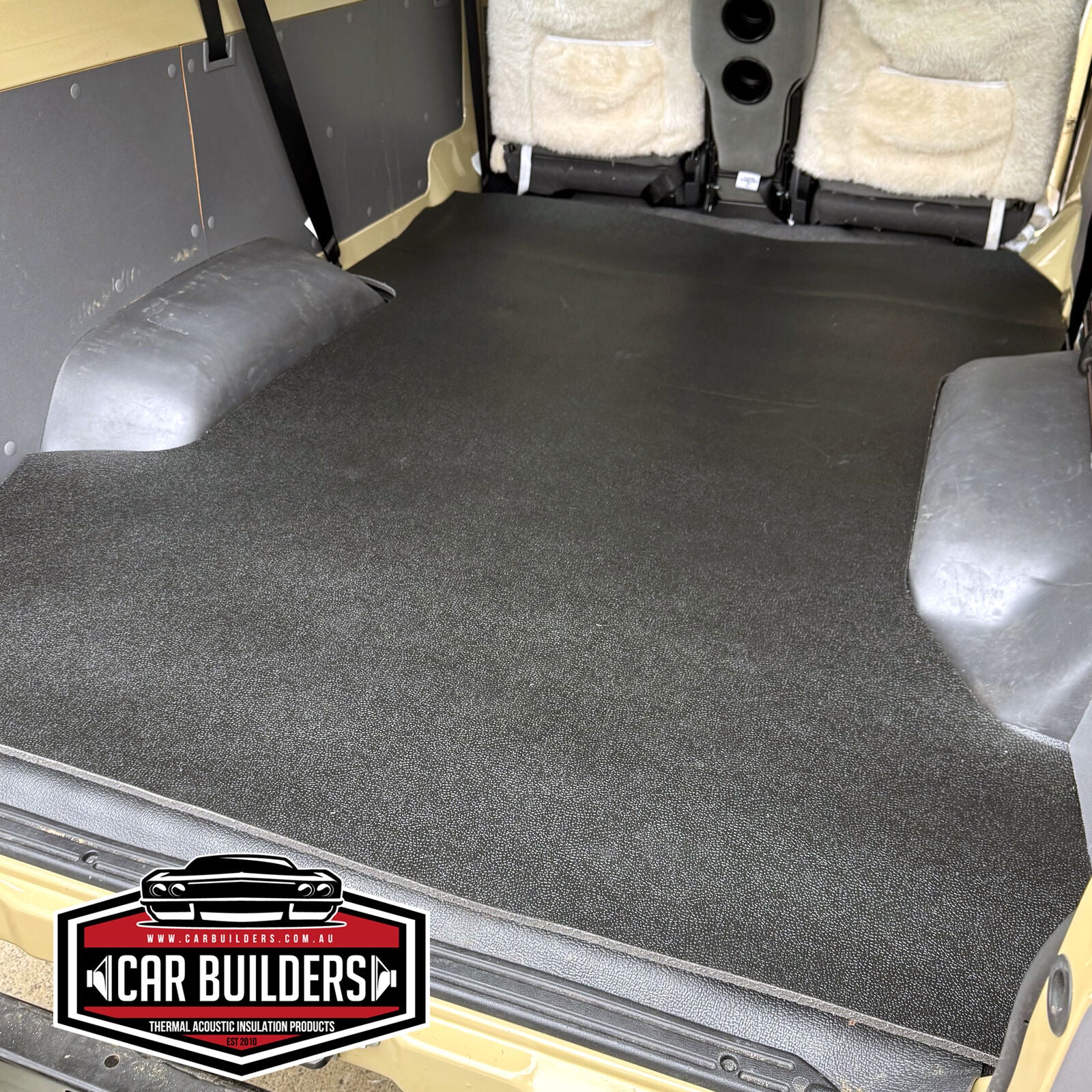 Black grained vinyl cargo mat laid across a Troopcarrier rear floor, shaped around both wheel arches up to the folded rear seats